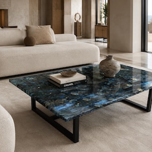 May include: A rectangular coffee table featuring a polished blue and black stone slab top with natural crystalline patterns, supported by a black metal frame. A small bowl, a book titled Chanel, and a textured vase sit on the surface.