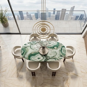 May include: An oval dining table with a green and white agate-patterned surface, surrounded by six cream-coloured upholstered chairs. Above the table hangs a gold circular pendant light fixture, positioned in a room with marble flooring and wood furniture.
