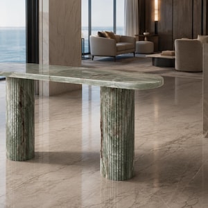 Puede incluir: Una mesa consola hecha de mármol verde con una superficie superior ovalada y alargada. La mesa está sostenida por dos columnas cilíndricas con estrías verticales que combinan con el mármol verde de la superficie.