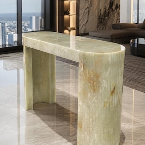 May include: A pale green stone console table with a smooth, polished top and a fluted, semi-circular base. The piece features natural veining and warm amber-colored inclusions throughout the translucent, light-reflecting surface.