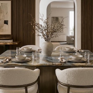Puede incluir: Una mesa de comedor cuadrada con una superficie de piedra pulida azul y marrón, rodeada por cuatro sillas texturizadas de color crema. La mesa está puesta con cuencos y platos de cerámica blanca, vasos transparentes y servilletas. Un jarrón texturizado contiene ramas.