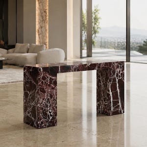 Pode incluir: Uma mesa consola retangular construída em mármore bordeaux profundo com veios brancos proeminentes. A peça apresenta uma silhueta geométrica limpa com duas pernas verticais espessas em forma de placa que suportam uma superfície plana.