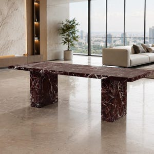 May include: A rectangular dining table crafted from deep red marble with prominent white veining. The table features a thick, flat top supported by two substantial, matching rectangular marble slab legs, creating a solid and monolithic appearance.
