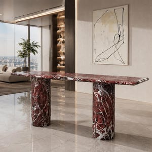 May include: A long console table crafted from deep red marble with prominent white veining. The table features a rectangular top supported by two thick, cylindrical marble columns, showcasing a polished, reflective surface throughout the piece.