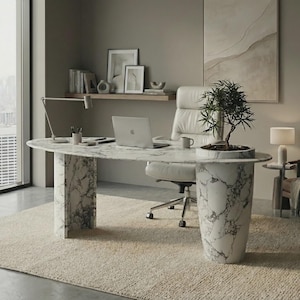 May include: An oval white marble desk with grey veining, supported by two cylindrical and rectangular pedestals. The desk features an integrated circular planter holding a small green tree, a silver laptop, a desk lamp, and a mug.