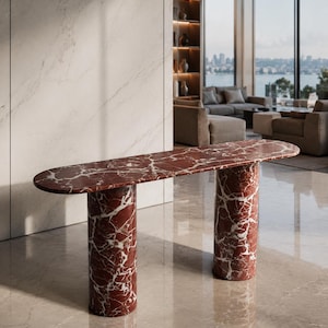 May include: A console table crafted from deep red marble with prominent white veining. The piece features an elongated, oval-shaped top supported by two thick, cylindrical columns, showcasing a polished stone finish throughout the entire structure.