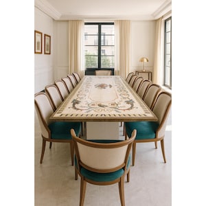 Puede incluir: Una mesa de comedor rectangular larga con una superficie de piedra clara que presenta un intrincado patrón de incrustaciones florales y de volutas. La mesa está rodeada por doce sillas con marcos de madera, respaldos crema y cojines azul cerceta.