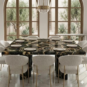 Puede incluir: Una mesa de comedor cuadrada con un tablero de piedra de ágata negra y dorada, con una superficie pulida y vetas naturales. La mesa está rodeada por ocho sillas tapizadas de color crema con patas finas de metal dorado sobre un suelo de mármol blanco.