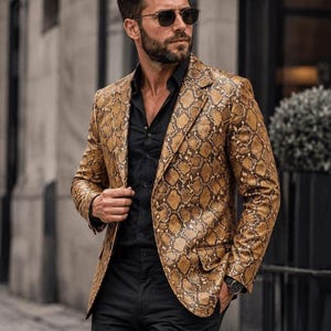 May include: A tan and brown snakeskin patterned blazer with notched lapels and two front flap pockets, worn over a solid black button-down shirt with black trousers, dark sunglasses, and a black wristwatch on the left wrist.