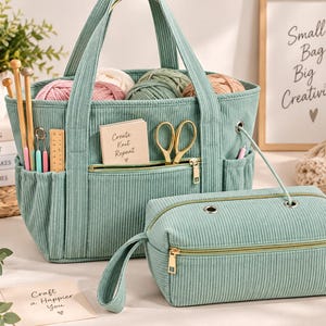 May include: A sage green corduroy craft tote bag and a matching rectangular zippered pouch. The tote features exterior pockets holding wooden knitting needles, crochet hooks, and scissors. A small notebook reads Create Knit Repeat.