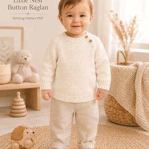 Op de afbeelding: Een crèmekleurige gebreide trui met lange mouwen, raglanmouwen en twee kleine bruine knoopjes op de linkerschouder. De tekst Little Nest Button Raglan Knitting Pattern PDF is zichtbaar in de linkerbovenhoek van de afbeelding.