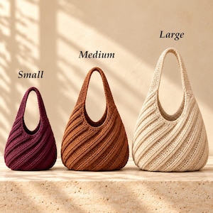 May include: Three crochet hobo bags in small, medium, and large sizes. The small bag is dark burgundy, the medium bag is rust orange, and the large bag is cream. Each bag features a diagonal ribbed texture and a single integrated handle.