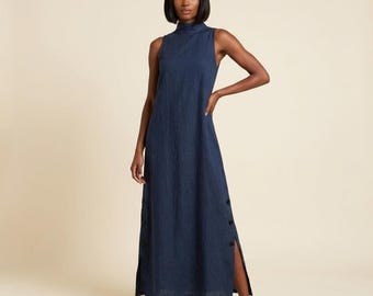Vestido largo de lino, sin mangas, con cuello alto y aberturas laterales con botones.