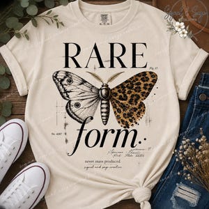 May include: A cream-colored t-shirt featuring a graphic of a moth with one wing in a black and white sketch style and the other in a brown leopard print. The text reads RARE form, Fig. 17, No. 4287, never mass produced, and signal and sage creative.