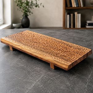May include: A rectangular wooden serving tray featuring a textured, dimpled surface pattern across the top. The tray is crafted from light brown wood with visible grain and is supported by four small, short wooden feet attached to the underside.