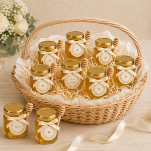 Peut inclure: Un panier en osier tressé contenant huit petits pots en verre de miel doré, chacun surmonté d'un couvercle doré, d'un ruban crème et d'une cuillère à miel en bois. Chaque pot porte une étiquette circulaire avec une couronne dorée.