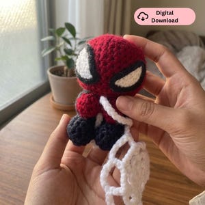 Puede incluir: Una pequeña muñeca de ganchillo hecha a mano con cabeza roja, grandes ojos blancos delineados en negro, torso rojo y piernas azul oscuro. Un accesorio de ganchillo blanco en forma de red está unido a la figura. Incluye la etiqueta Digital Download.