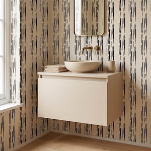 Puede incluir: Un mueble de lavabo suspendido en color beige claro cuenta con un lavabo redondo y un grifo de latón. Las paredes están cubiertas con papel pintado de rayas verticales negras. Un espejo rectangular cuelga sobre el lavabo.