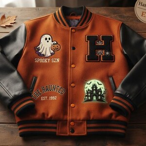 May include: An orange varsity jacket with black sleeves, featuring a ghost holding a pumpkin, the text SPOOKY SZN, a large letter H, the text THE HAUNTED EST. 1992, and a haunted house graphic. The jacket has a button-up front and striped ribbed trim.