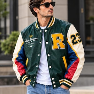 Könnte beinhalten: Eine Collegejacke mit dunkelgrünem Rumpf und Ärmeln in Creme, Blau und Rot. Auf der Vorderseite steht der Text New Horizons EST. 2020 mit einem Kronensymbol, einem großen gelben Buchstaben R und der Zahl 23 auf dem Ärmel. Mit weißen Druckknöpfen.