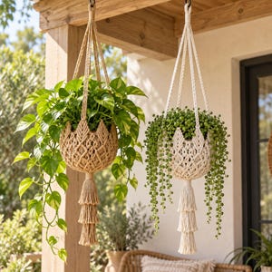 Puede incluir: Dos soportes de macramé para plantas colgados de una viga de madera. El soporte izquierdo es de color tostado con una planta potos, y el derecho es de color blanco roto con una planta rosario. Ambos tienen nudos complejos y borlas escalonadas.