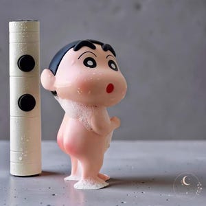Puede incluir: Una pequeña figura de personaje de dibujos animados de piel clara, con cabello negro grueso y boca roja, cubierta de burbujas de jabón blancas. Junto a la figura hay un objeto cilíndrico de color blanco roto con dos botones negros.