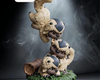 Pode incluir: Uma estatueta decorativa com três criaturas empilhadas de cor creme com marcas de seta cinzento-escuras nas cabeças, pousadas numa base de relva verde junto a um tronco de madeira castanho. O texto Bestseller é visível num retângulo.