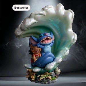 May include: A decorative figurine featuring a blue alien character and a small girl with dark hair in a red dress, positioned in front of a large, translucent, light green wave. The base includes coral and rock details with the text Bestseller.