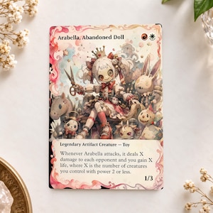 May include: A rectangular trading card titled Arabella, Abandoned Doll, featuring a central doll character with button eyes, a crown, and scissors, surrounded by various small toy creatures, with game text and a 1/3 power and toughness.