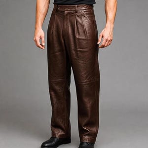 Puede incluir: Pantalones de cuero marrón oscuro con diseño de cintura alta, pliegues frontales, cierre de botón en la cintura y costuras horizontales en las rodillas. Los pantalones tienen un corte recto y un acabado liso y pulido.