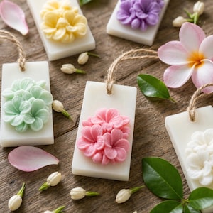 May include: Five rectangular white wax tablets, each featuring a raised floral relief in yellow, purple, light green, pink, or white. Each tablet includes a jute twine loop at the top for hanging, surrounded by scattered jasmine buds, green leaves, and pink petals.
