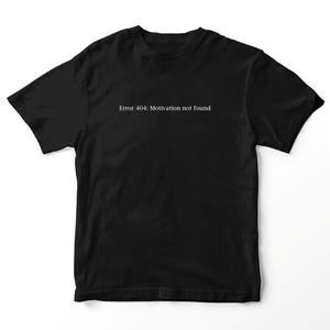 Op de afbeelding: Een zwart t-shirt met korte mouwen en de witte tekst "Error 404: Motivation not found" in het midden op de borst gedrukt. Het kledingstuk heeft een standaard ronde hals en een rechte zoom, wat zorgt voor een eenvoudig en strak ontwerp.