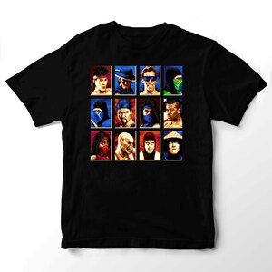 May include: A black short-sleeved t-shirt featuring a grid of twelve pixelated character portraits from the Mortal Kombat video game series. The graphic displays various fighters in distinct colors and headgear arranged in three rows of four squares.