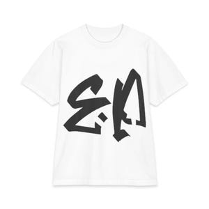 Może przedstawiać: Biały t-shirt z krótkim rękawem z dużym, wyrazistym czarnym nadrukiem graficznym na klatce piersiowej. Wzór składa się ze stylizowanych, kanciastych liter w stylu kaligraficznym, które wydają się być abstrakcyjne lub symboliczne i są wyśrodkowane.