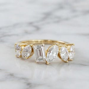 Peut inclure: Une bague en or jaune avec un diamant central taille émeraude, entouré de deux diamants taille marquise et de deux diamants taille ronde de chaque côté. L'anneau présente une disposition multi-pierres avec des gemmes transparentes et facettées.