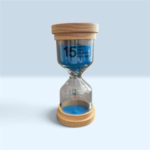 May include: A 15-minute hourglass with light wood end caps and bright blue sand. The glass chamber features the printed text 15 HAPPY TIME :) SandGlass minutes. The sand is currently collected in the top bulb, with a small amount flowing down.