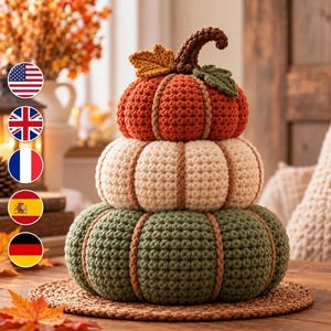 May include: A stacked pumpkin decoration made of crocheted yarn in three distinct colours. The top pumpkin is orange, the middle is cream, and the bottom is sage green. Each section features vertical ribbed detailing and a brown crocheted stem.