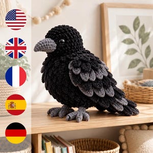 Pode incluir: Um peluche de corvo feito em croché com um corpo preto sólido e penas texturizadas em camadas em tons de preto e cinzento. A ave tem um bico cinzento, patas cinzentas e olhos pretos brilhantes, pousada sobre uma superfície de madeira.