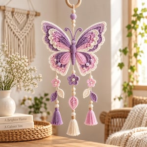 May include: A hanging crochet butterfly ornament in shades of purple, pink, and cream. The butterfly features intricate stitching, small beads, and three dangling strands adorned with crocheted flowers, leaves, wooden beads, and colorful tassels.