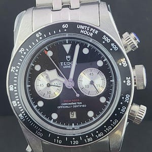 Puede incluir: Un reloj cronógrafo Tudor de acero inoxidable con esfera negra, subesferas plateadas y bisel taquimétrico. El reloj cuenta con una ventana de fecha en la posición de las seis, marcadores de hora luminosos y un brazalete de eslabones metálicos.