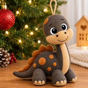May include: A felt dinosaur ornament featuring a dark gray body with tan accents on the face, chest, and feet. The dinosaur has orange circular spots on its back and a row of orange triangular plates along its spine, with a hanging loop at the top.