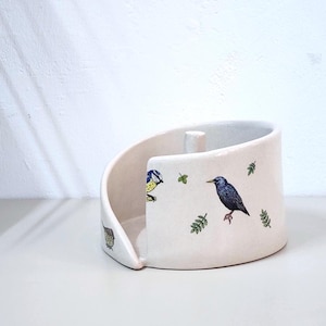 Pode incluir: Uma caneca de cerâmica branca com uma alça preta e o texto "But First, Coffee" em estilo manuscrito. A caneca está sobre uma superfície branca. A caneca tem aproximadamente 10 cm de altura.