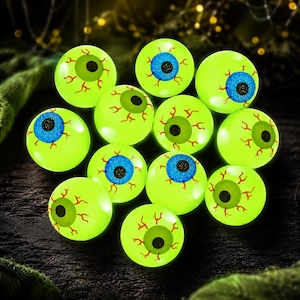 Op de afbeelding: Een verzameling van twaalf bolvormige oogboldecoraties met een fel neon-groene sclera en rode aders. Elke oogbol heeft een centrale iris in effen groen of glinsterend blauw, die een zwarte ronde pupil omringt.