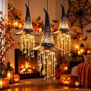 May include: Three black witch hat light fixtures suspended from above, each featuring a textured, pointed crown with a buckle band and cascading strings of glowing warm white LED lights adorned with small star-shaped ornaments.