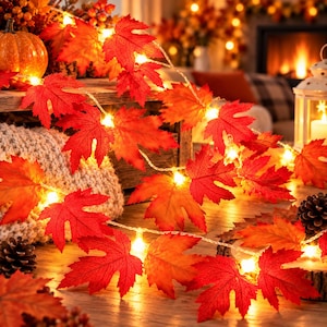 Peut inclure: Une guirlande lumineuse décorative composée de feuilles d'érable artificielles dans des tons de rouge, orange et jaune. Les feuilles sont entremêlées de petites ampoules LED à lumière chaude, créant un effet lumineux sur le feuillage.