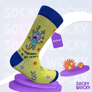 May include: A yellow crew sock with a blue cuff, heel, and toe. The sock features a cartoon purple cell character, DNA strands, and the text "I'M OVEREATING IT'S IN MY GENES!" along with various scientific icons like atoms and viruses.