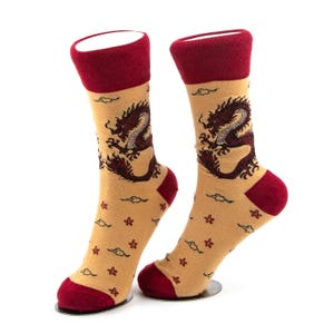 Könnte beinhalten: Ein Paar Socken mit beigefarbener Basis und einer dunkelroten Drachengrafik im oberen Bereich. Der untere Teil der Socken zeigt ein wiederkehrendes Muster aus kleinen roten Blumen und dunklen Wolken. Die Bündchen, Fersen und Zehen sind dunkelrot.