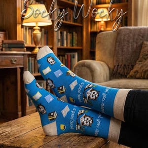 Può includere: Calzini blu brillante con un motivo ripetuto di gufi che leggono libri, pile di libri e tazze gialle. Il testo "Socky Wocky" appare in alto e la frase "all you need is a good book" è stampata sul lato dei calzini.