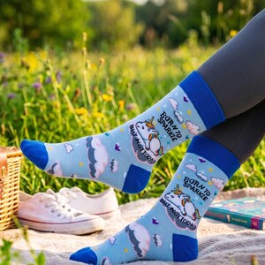 Könnte beinhalten: Hellblaue Socken mit einem Einhorn-Motiv mit regenbogenfarbener Mähne, rosa-weißen Wolken und gelben Sternen. Der Text "BORN TO SPARKLE" und "BEAT NOT TODAY" ist auf die Socken gedruckt. Die Socken haben einfarbig blaue Bündchen und Zehenbereiche.