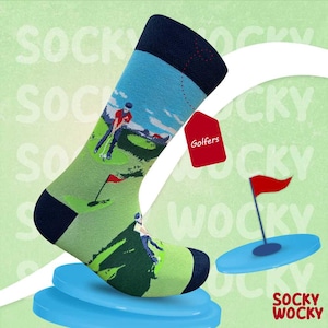 Könnte beinhalten: Ein wadenlanger Socken mit einem hellgrünen Golfplatz-Motiv und darauf abgebildeten Golfspielern in Bewegung. Der Socken hat ein dunkelblaues Bündchen sowie eine dunkelblaue Ferse und Spitze. Ein rotes Etikett mit dem weißen Text "Golfers" ist angebracht.